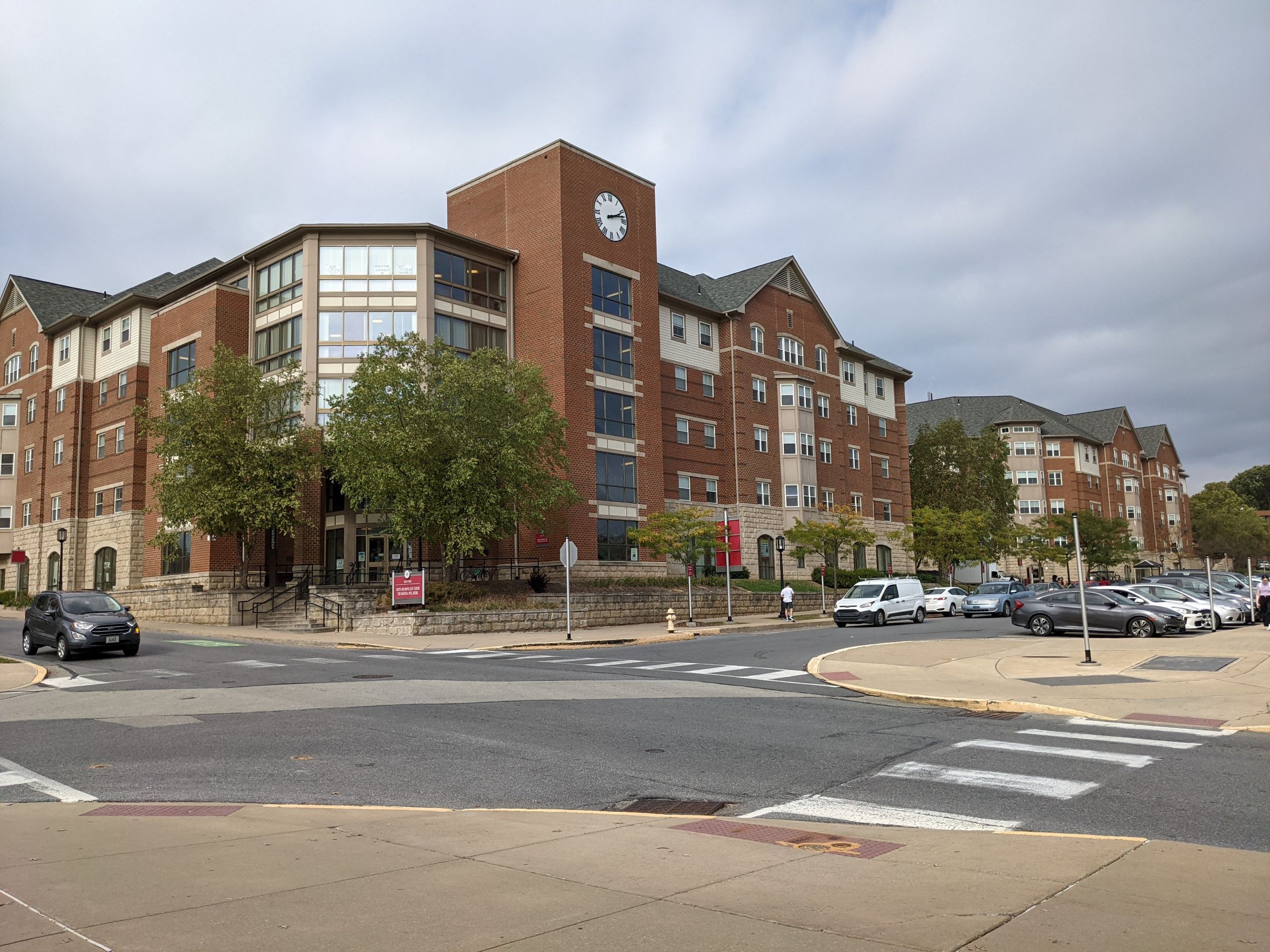 Traditional looking five story red brick living learning student housing community dormitory building with large clock tower overlooking large campus intersection