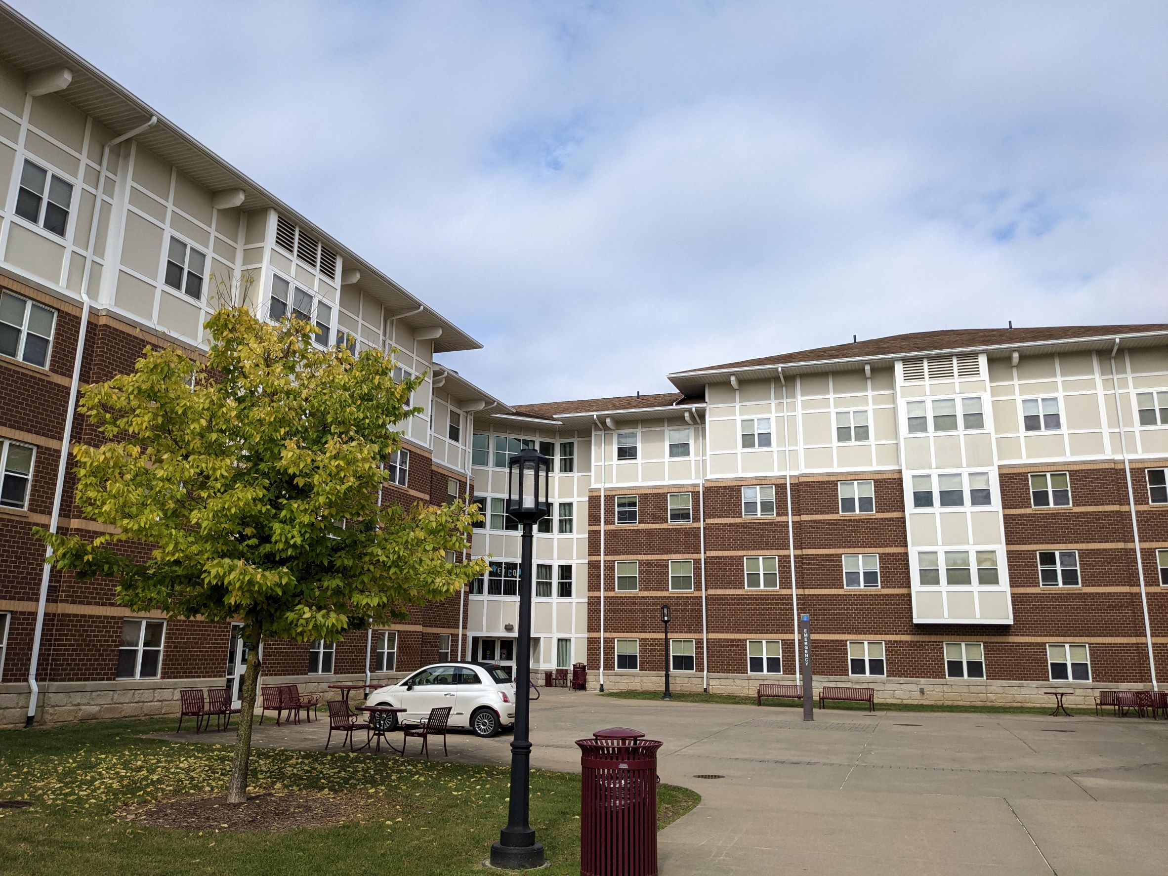 Modern stylized arts & crafts residence hall with brown brick, beige tudor looking siding with white accents and big roof overhangs