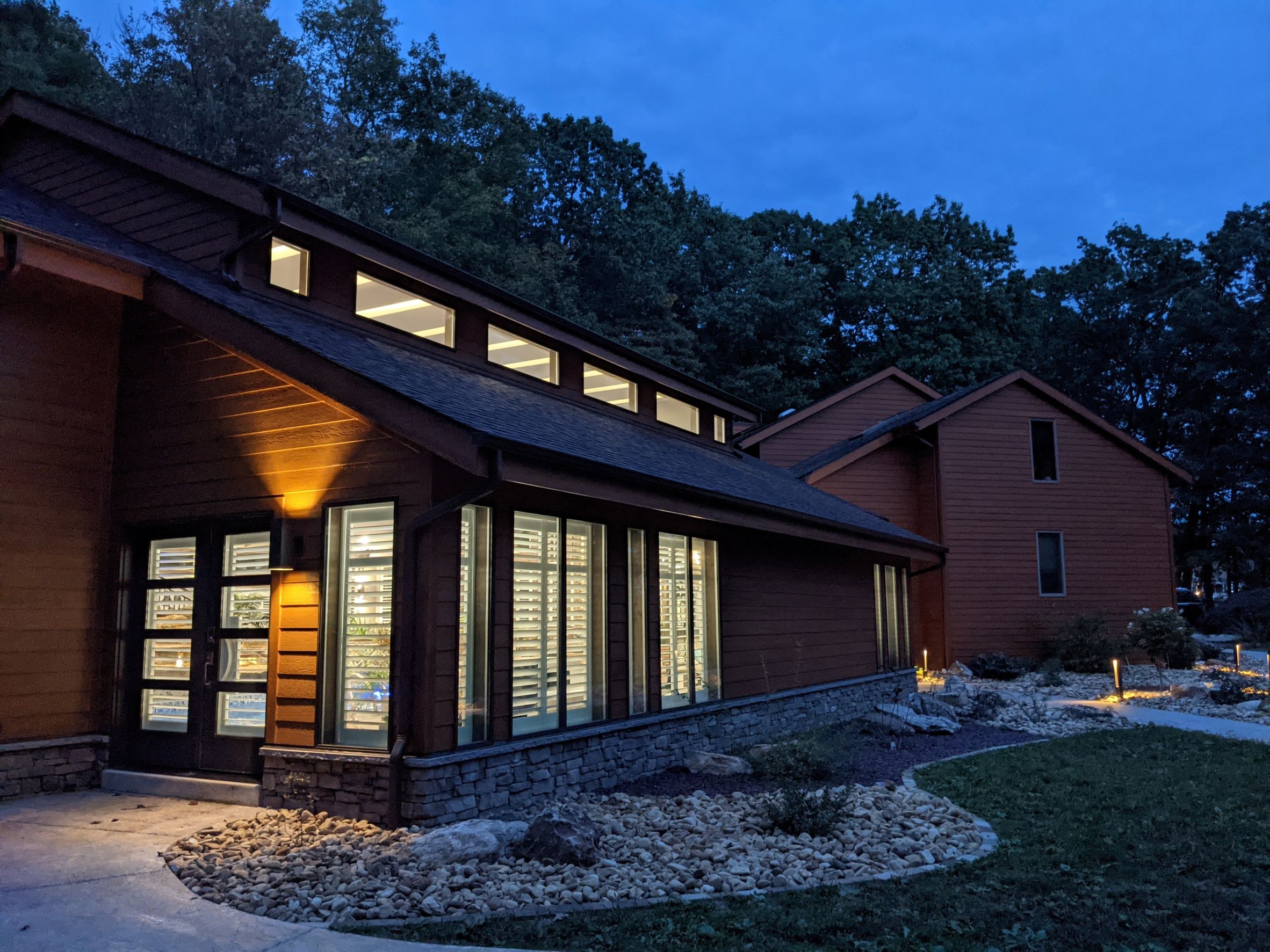 Exterior View of Contemporary House addition with stone, wood siding for an indoor pool at dusk with light spilling out of windows outside of Pittsburgh Pennsylvania